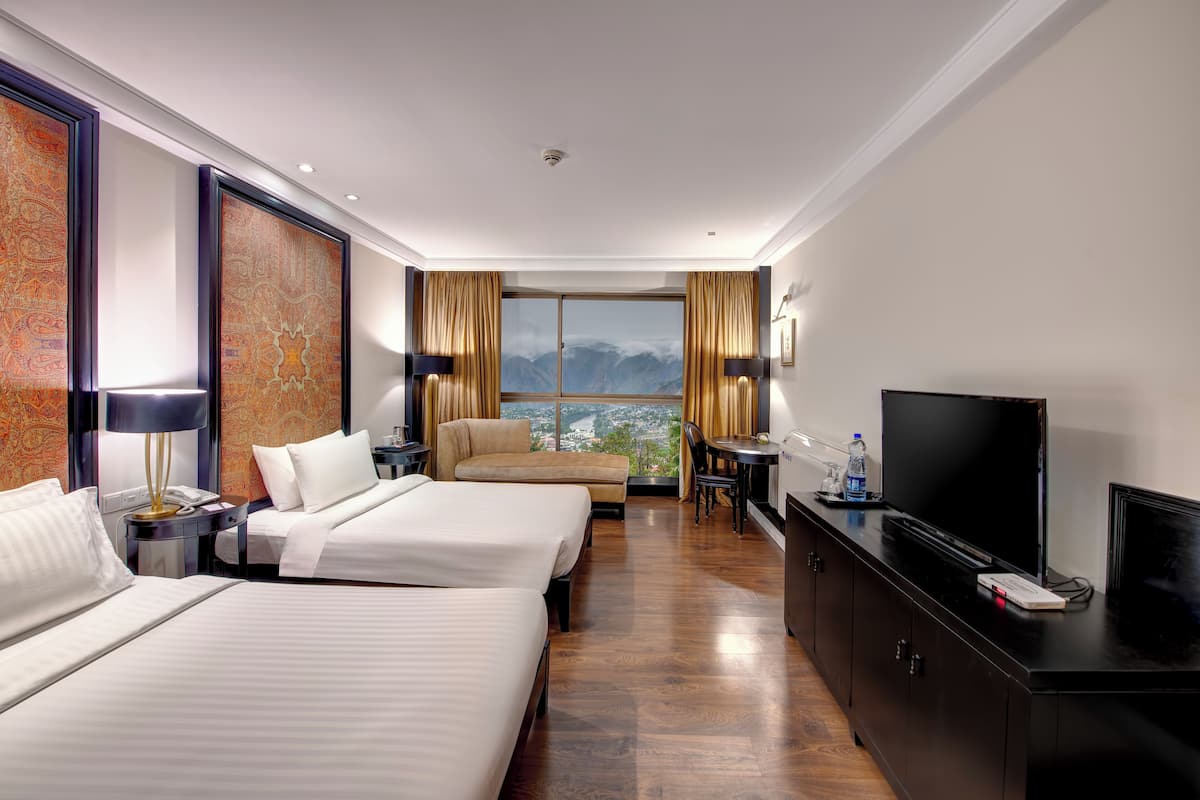Une chambre d’hôtel avec deux lits, une télévision, un bureau avec une chaise et une vue sur les montagnes par la fenêtre.