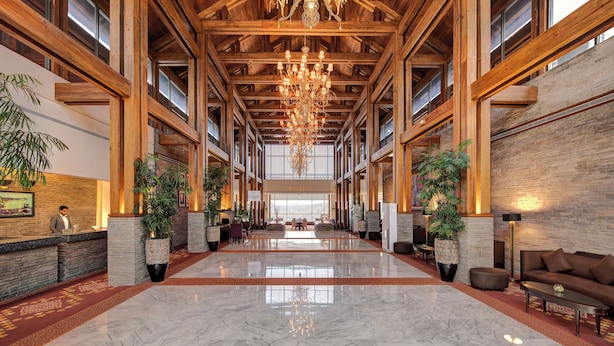 A spacious lobby with a high ceiling, wooden beams, a chandelier, and a marble floor.