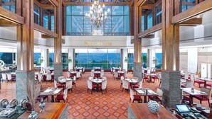 A spacious dining area with high ceilings, wooden beams, and large windows offering a view of the outdoors.