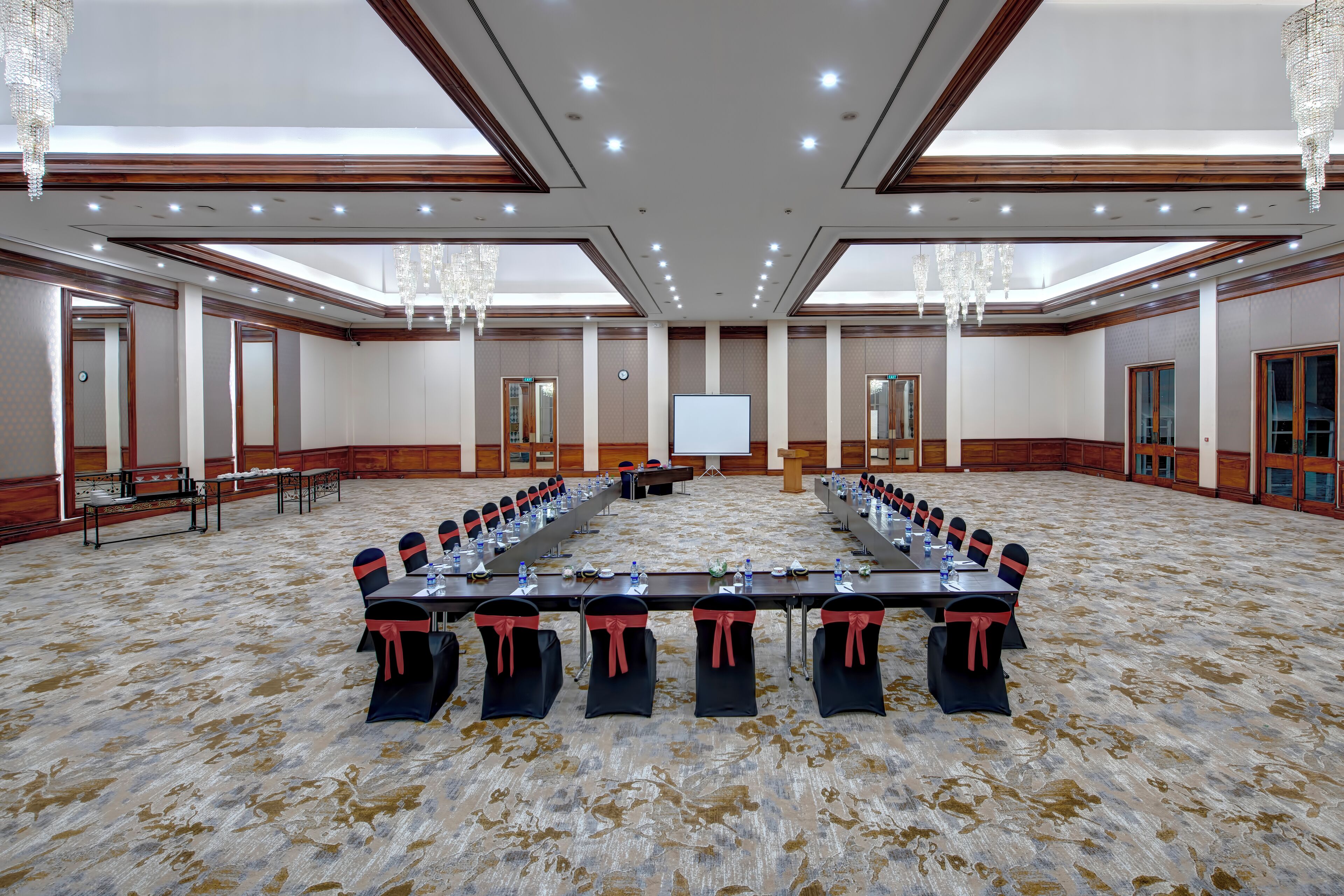 A large conference room with a long table, chairs with red sashes, and a projector screen.