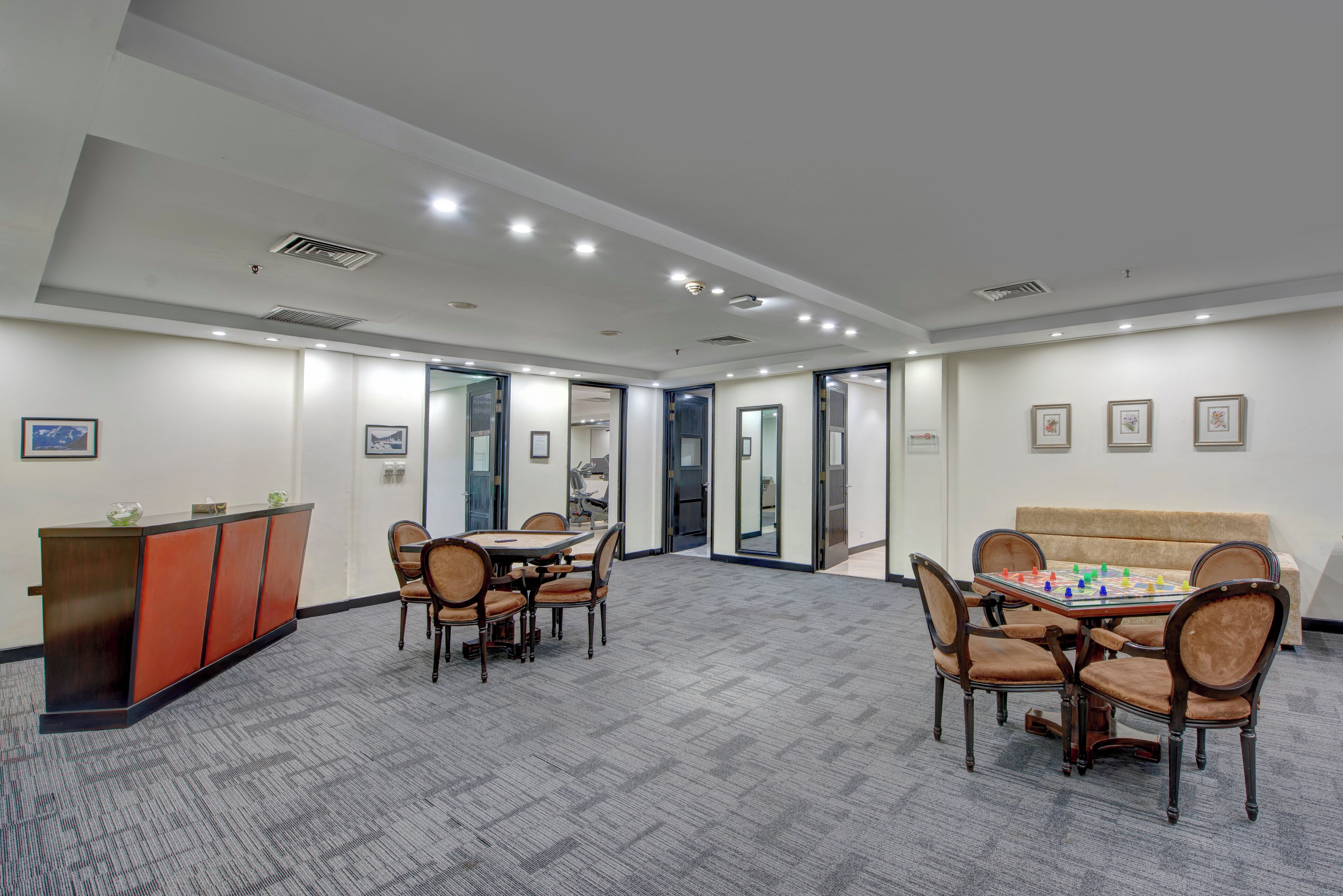 A spacious room with a carpeted floor, a reception desk, a dining table with chairs, and a sofa.