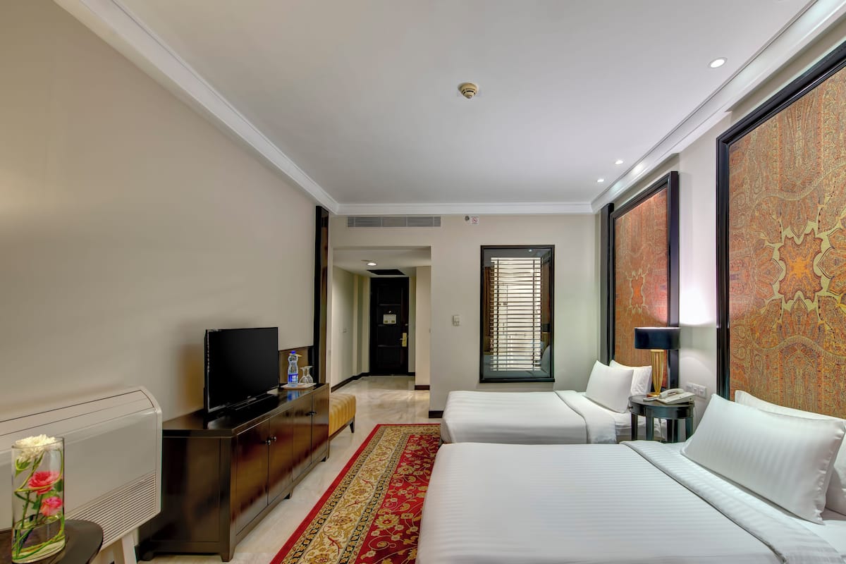 Une chambre d’hôtel avec deux lits, une télévision, un bureau et un tapis décoratif.