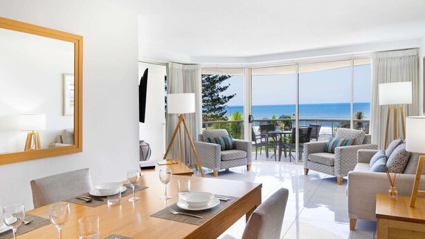 A modern hotel room with a dining area, a sofa set, and a large window offering a view of the sea. - Mantra Zanzibar (Mooloolaba)