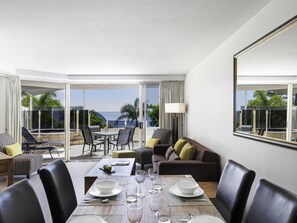 Habitación de hotel con comedor, sofá y una ventana grande con vista al océano.