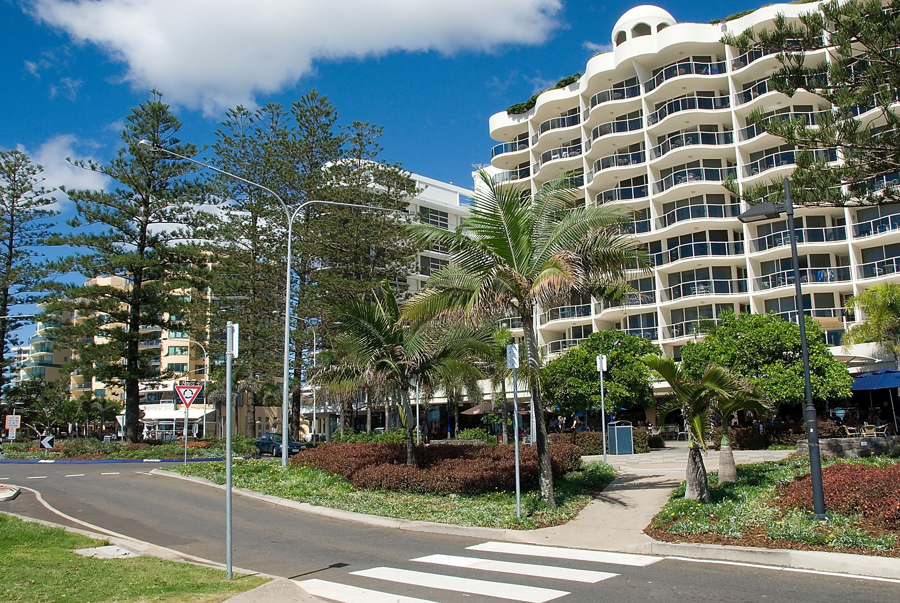 A multi-story hotel with balconies, surrounded by greenery and a pedestrian crossing.