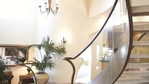 A modern interior with a curved staircase, a chandelier, and a seating area with a large potted plant. - Mantra Zanzibar (Mooloolaba)