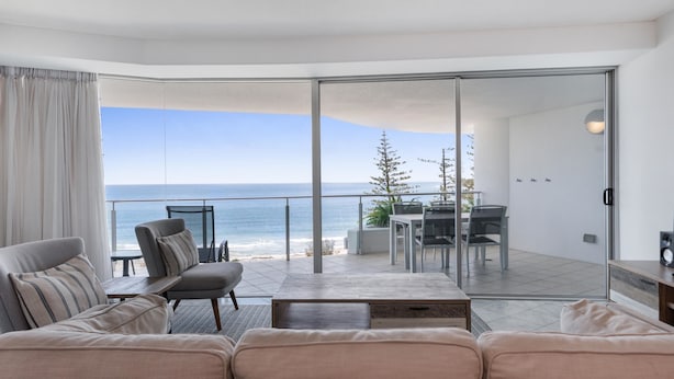 A modern living room with a sofa, chairs, a coffee table, and a view of the ocean through large glass doors. - Mantra Sirocco Resort (Mooloolaba)