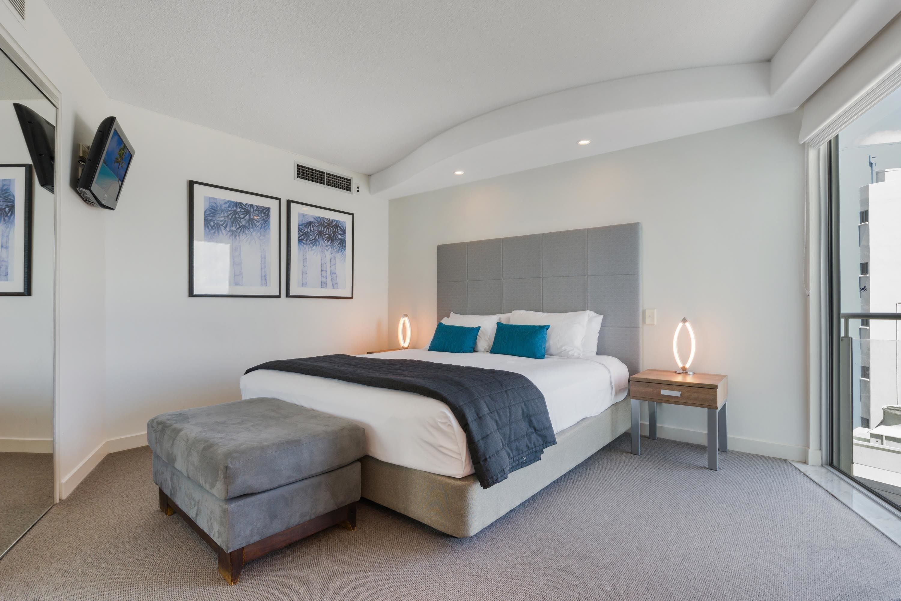 A modern bedroom with a large bed, bedside tables, and artwork on the walls.