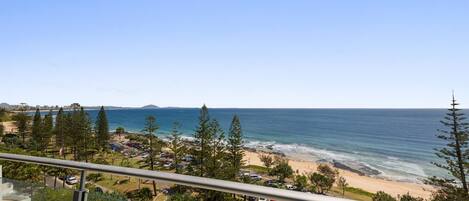 A balcony with a view of a beach, ocean, and distant mountains.
