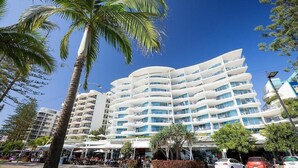 A multi-story hotel with a curved facade, outdoor seating area, and palm trees. - Mantra Sirocco Resort (Mooloolaba)