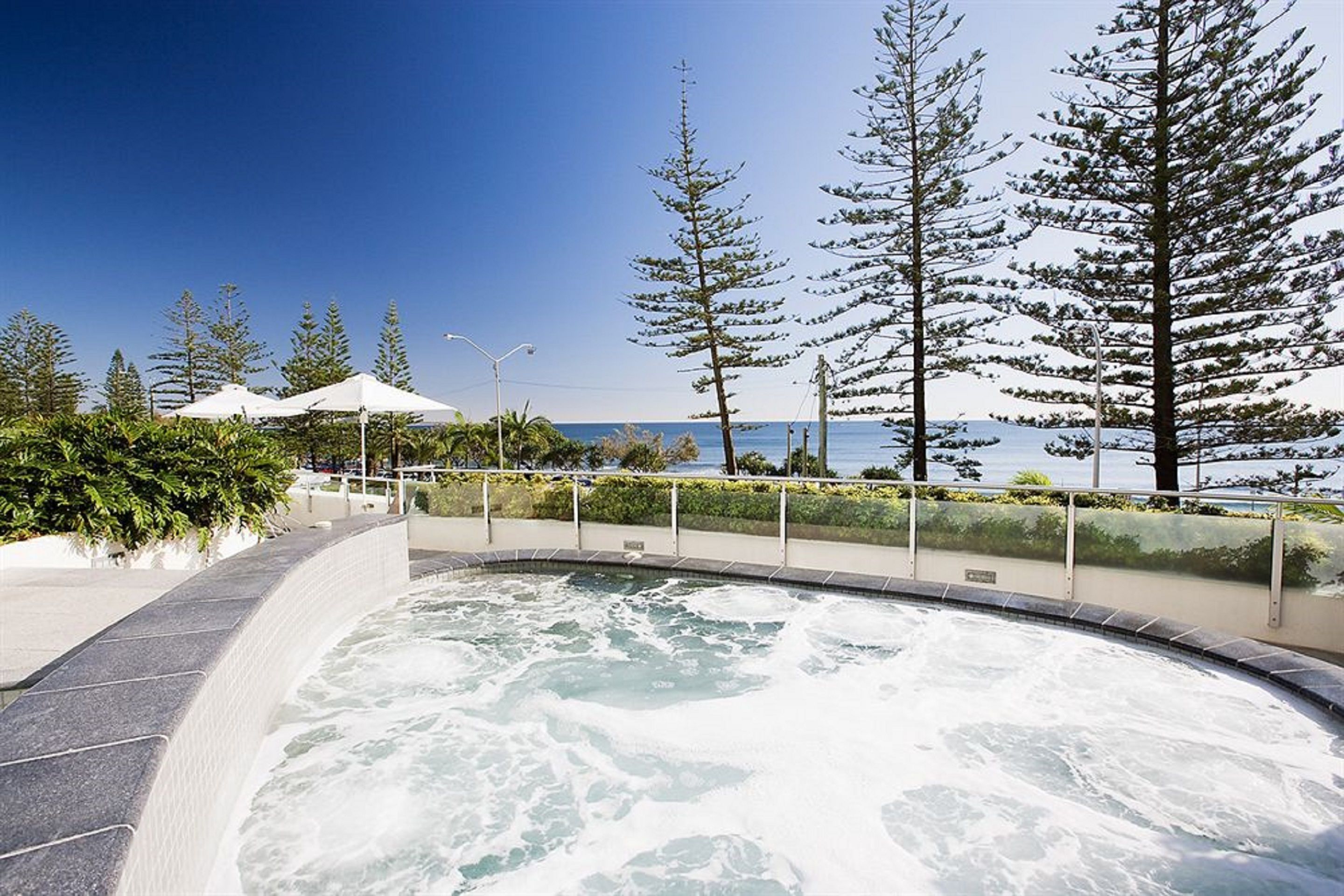 A hot tub area with a curved edge, surrounded by a railing, and overlooking a body of water with trees in the background.