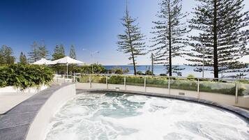 A hot tub area with a curved edge, surrounded by a railing, and overlooking a body of water with trees in the background.