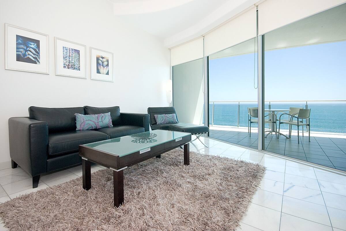 A modern living room with a glass door leading to a balcony with a view of the sea.