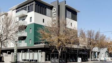 A modern building with a green and white facade, a visible entrance, and a covered outdoor seating area.