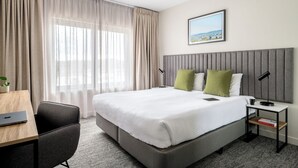 A modern hotel room with a large bed, a desk, a chair, and a view of the city through the window. - Quest Albury (Albury)