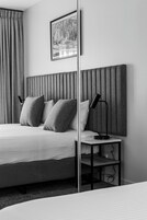 Una habitación de hotel moderna con una cama grande, un cabecero con líneas verticales, dos lámparas de noche y un cuadro enmarcado en la pared.