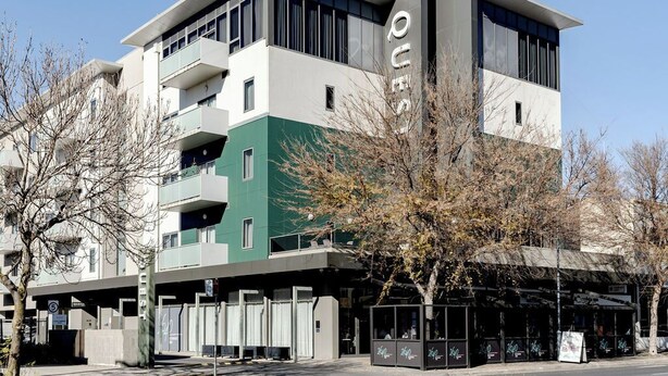 A modern building with a green and white facade, multiple balconies, and a covered entrance area.