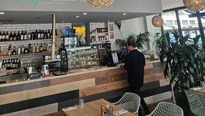 A restaurant interior with a bar area, wooden flooring, hanging wicker chandeliers, and a visible menu board. - Quest Albury (Albury)