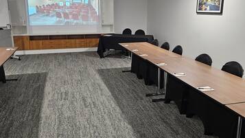 A conference room with a long table, chairs, a projector screen, and a carpeted floor.