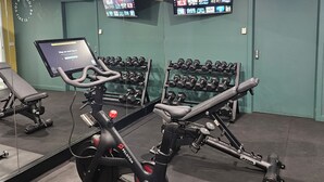 A gym with exercise equipment, including treadmills and dumbbells, and a TV screen displaying fitness content.