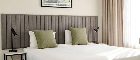 A neatly made bed with a grey headboard, two bedside tables with lamps, and a framed picture on the wall.