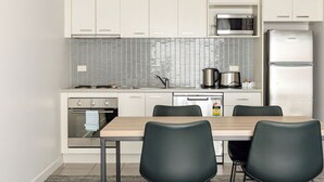 A modern kitchen with white cabinets, a microwave, a stainless steel refrigerator, a stove, and a dishwasher. There is a wooden table with four chairs.