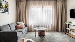 A modern living room with a grey sofa, a round coffee table, and a TV on a stand. - Quest Albury (Albury)
