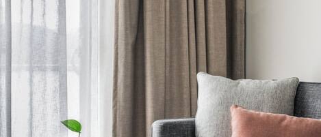 Una sala moderna con un sofá gris, una mesa de centro redonda y un ventanal con cortinas translúcidas.