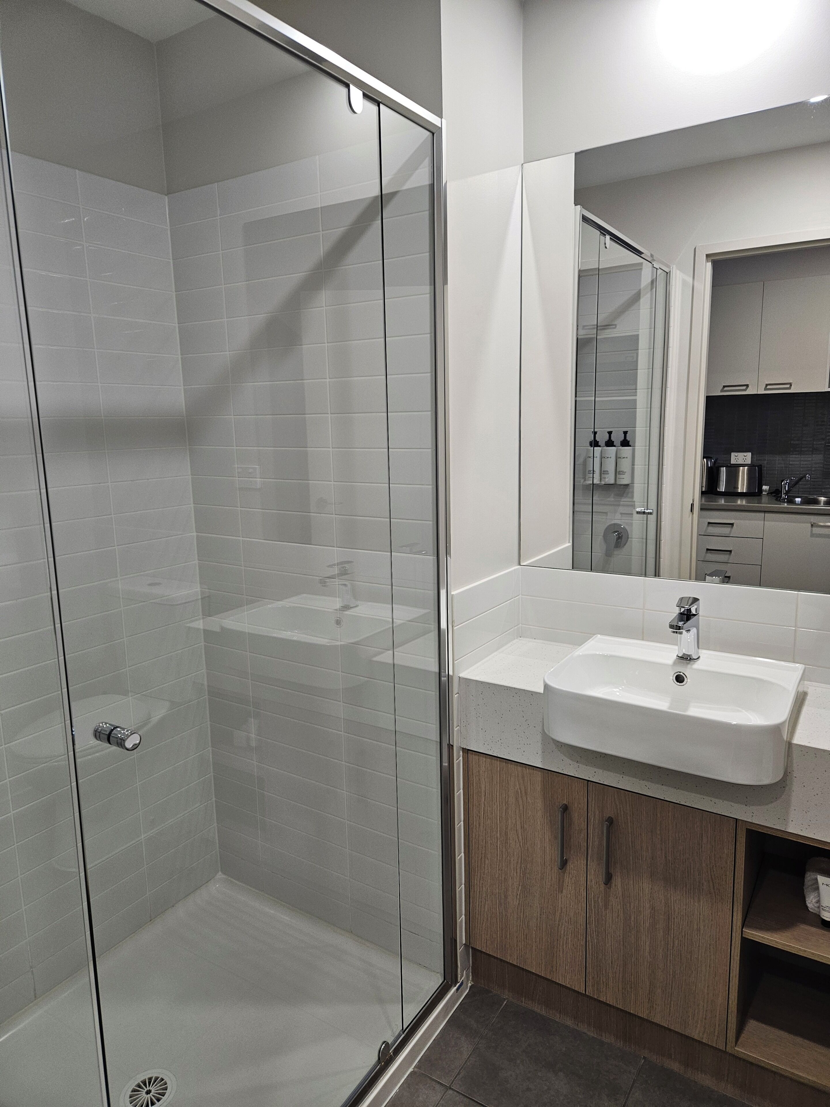 A modern bathroom with a glass-enclosed shower, a white sink, and wooden cabinets.