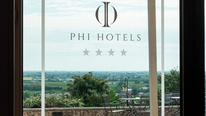 Una ventana de vidrio con el logotipo y el nombre de PHI HOTELS, vista a un patio con mesas al aire libre y un paisaje de fondo.