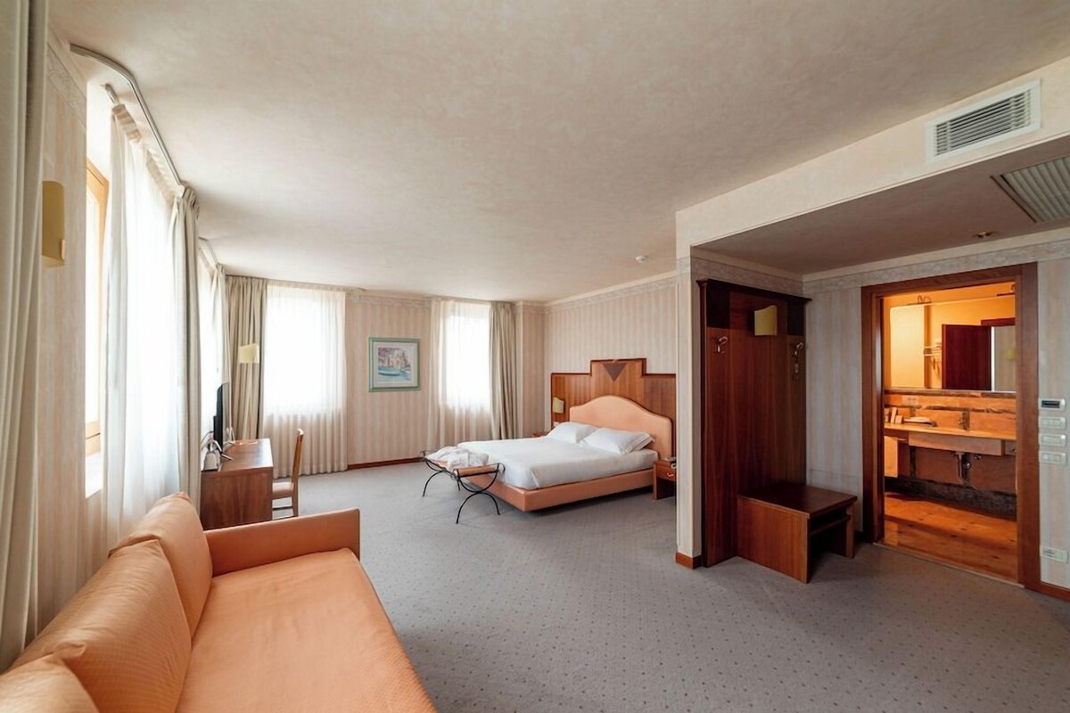 A hotel room with a bed, a sofa, a desk, a mirror, and a bathroom.