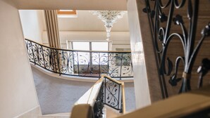 Una escalera con barandillas negras ornamentales, un candelabro y vista del piso superior.