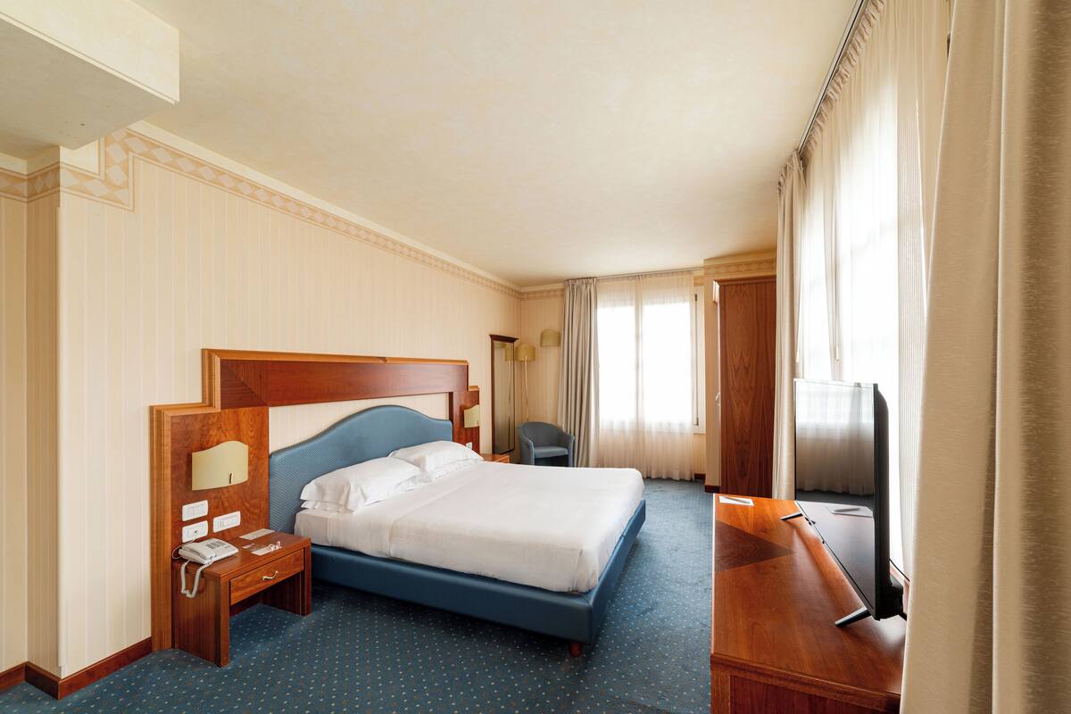 A hotel room with a bed, a desk, a chair, a TV, and a phone on a nightstand.