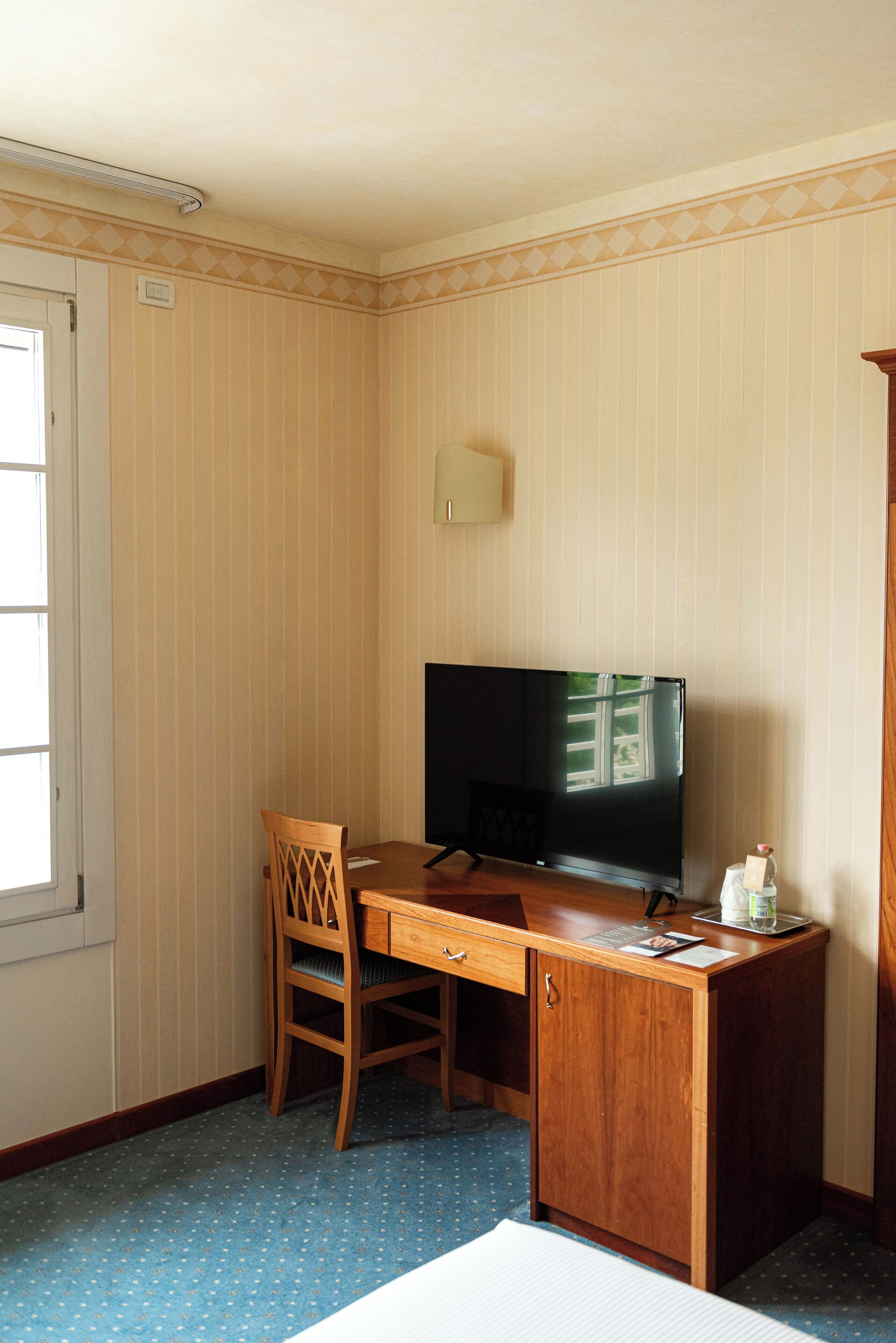 Una habitación de hotel con un escritorio de madera, televisión, una silla y un armario pequeño.