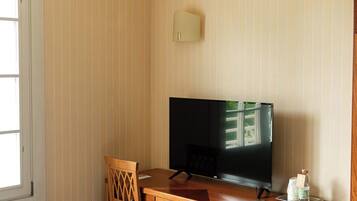 Una habitación de hotel con un escritorio de madera, televisión, una silla y un armario pequeño.