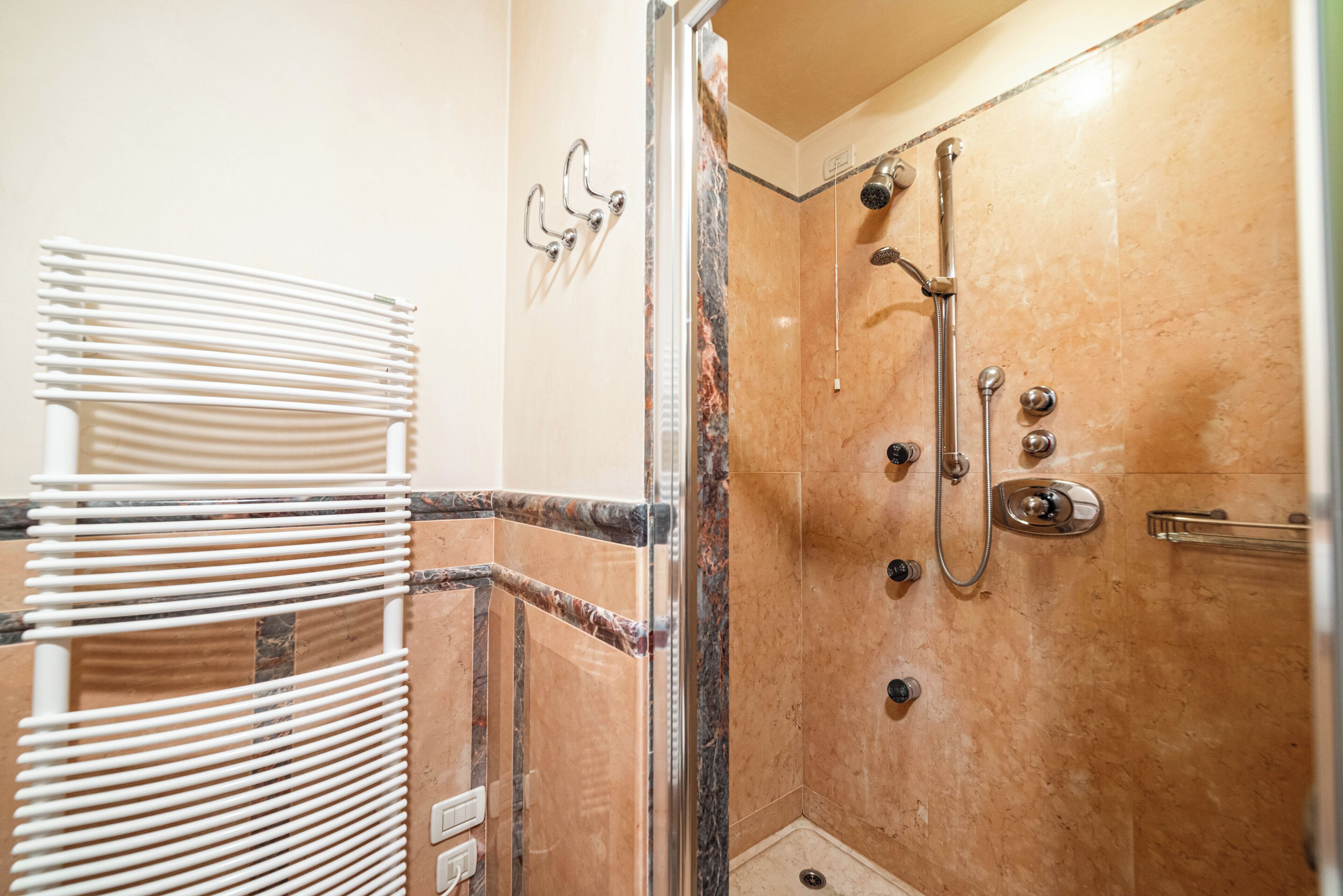 A shower with a glass door, a towel rack, and a marble wall.