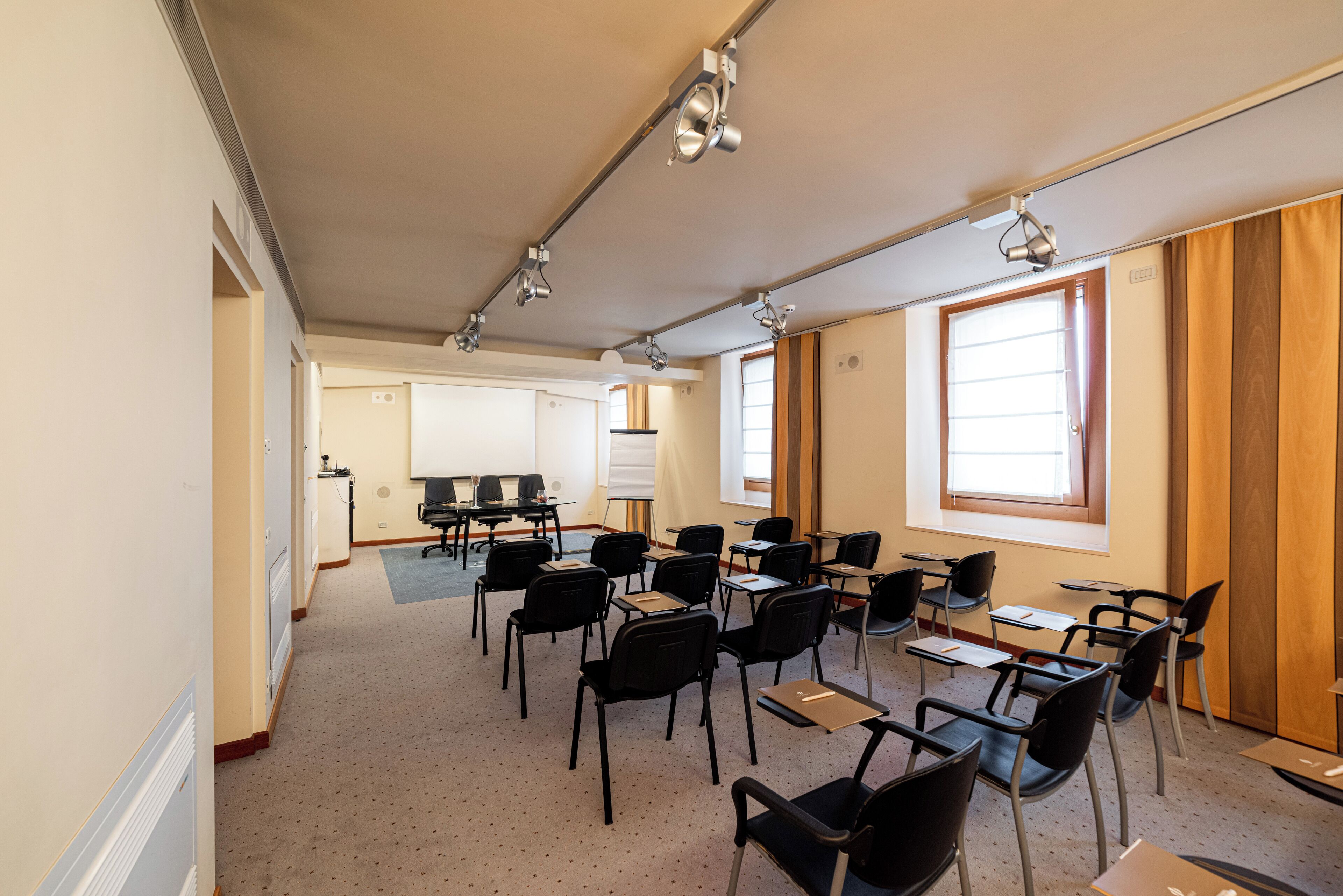 Une salle de conférence équipée de tables et de chaises, d’un tableau blanc et d’un projecteur.