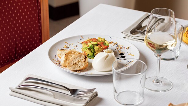Una mesa de comedor con un plato de comida, una copa de vino blanco y cubiertos.