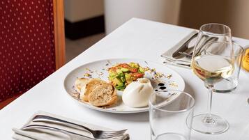 Una mesa de comedor con un plato de comida, una copa de vino blanco y cubiertos.