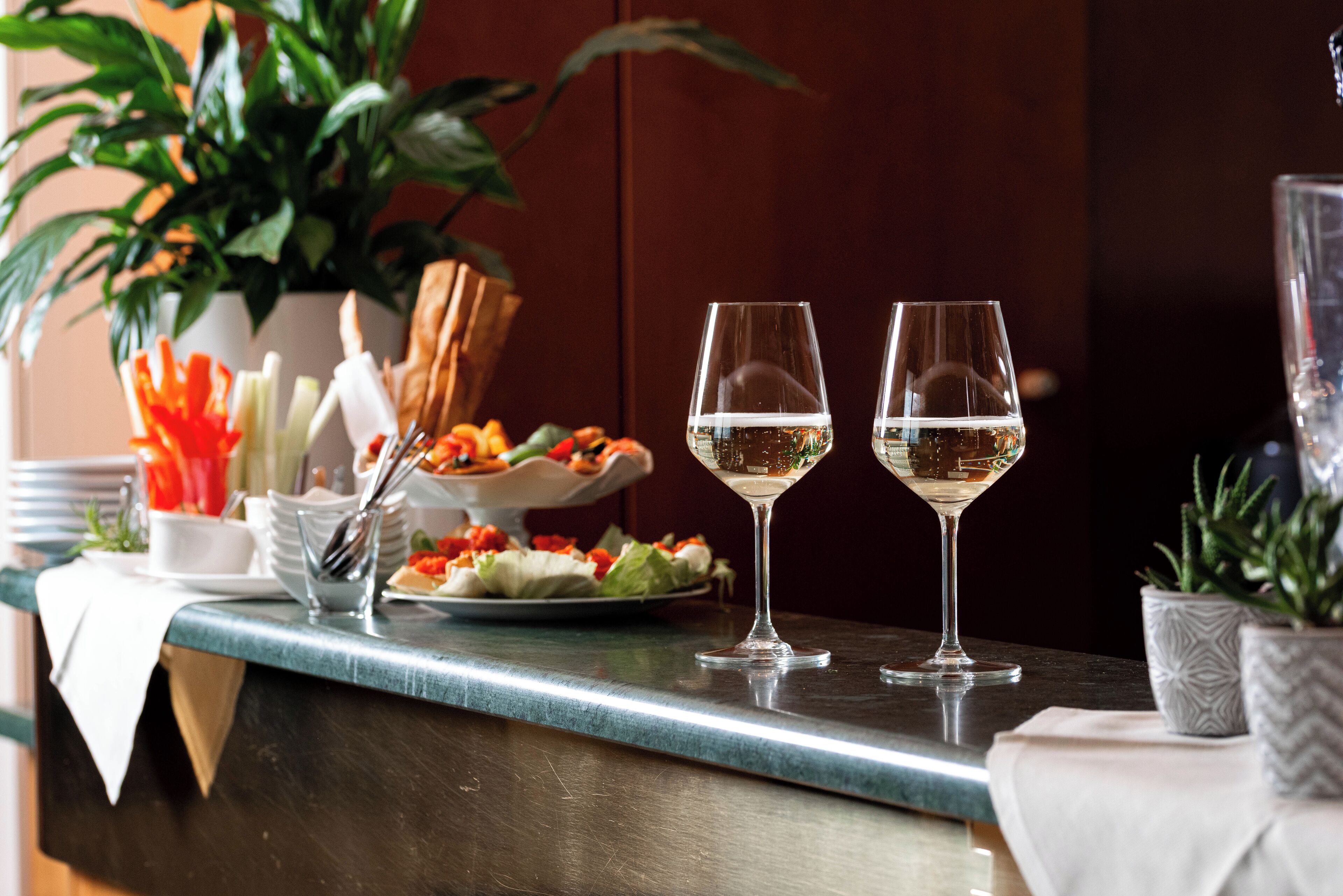 A bar area with two glasses of white wine, a plate of food, and a potted plant.