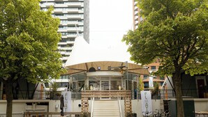 Un bâtiment moderne doté d’un espace extérieur couvert, entouré d’arbres et bordé d’immeubles de grande hauteur.