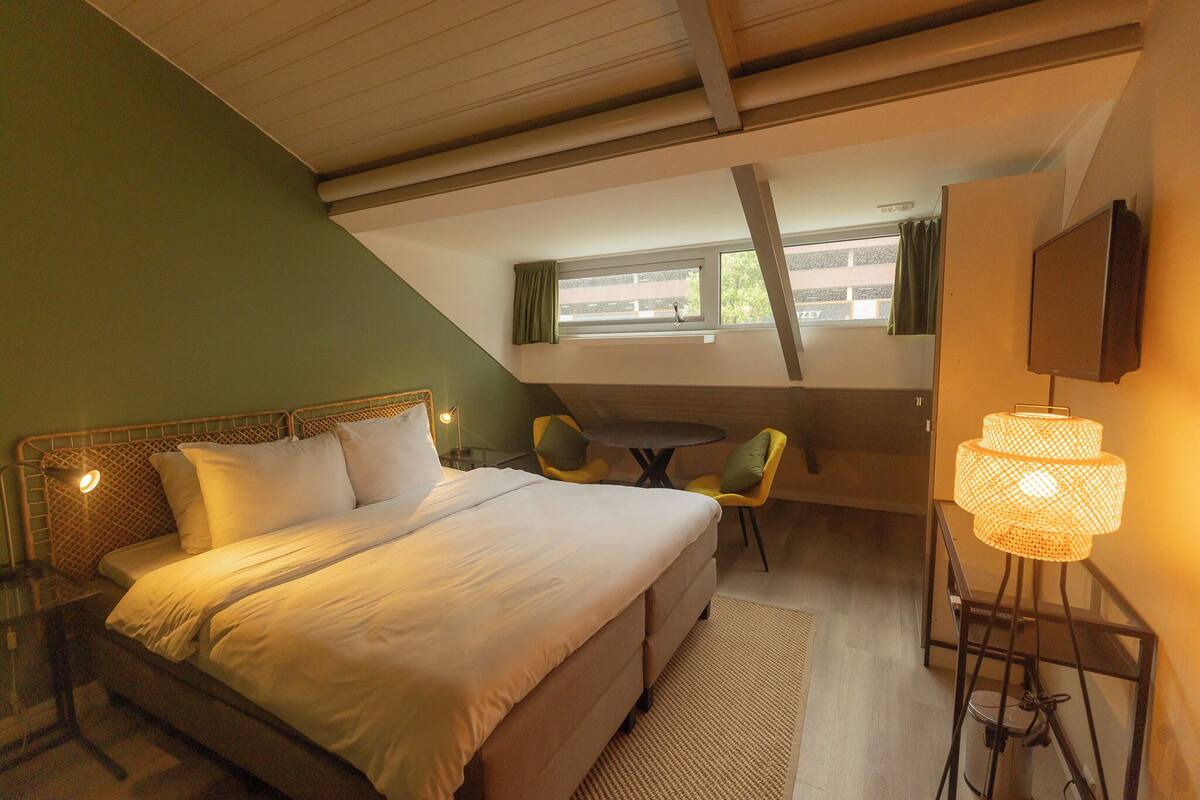 A bedroom with a bed, a desk, a chair, a lamp, and a window.