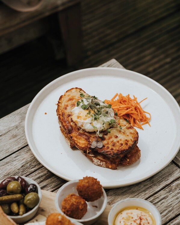 A plate with a slice of grilled cheese sandwich, sprouts, and shredded carrots on a wooden table.