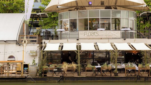 Un restaurant situé au bord de l’eau, doté d’une terrasse, de grandes fenêtres et d’une enseigne indiquant « Restaurant Flores ».