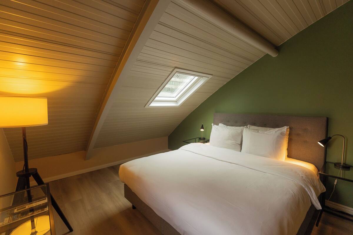 A bedroom with a skylight, a bed, bedside tables, and a lamp.