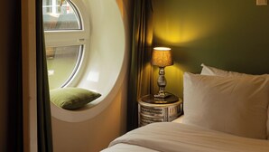 Une chambre d’hôtel avec un lit, une fenêtre ronde, une lampe et un appareil de climatisation.