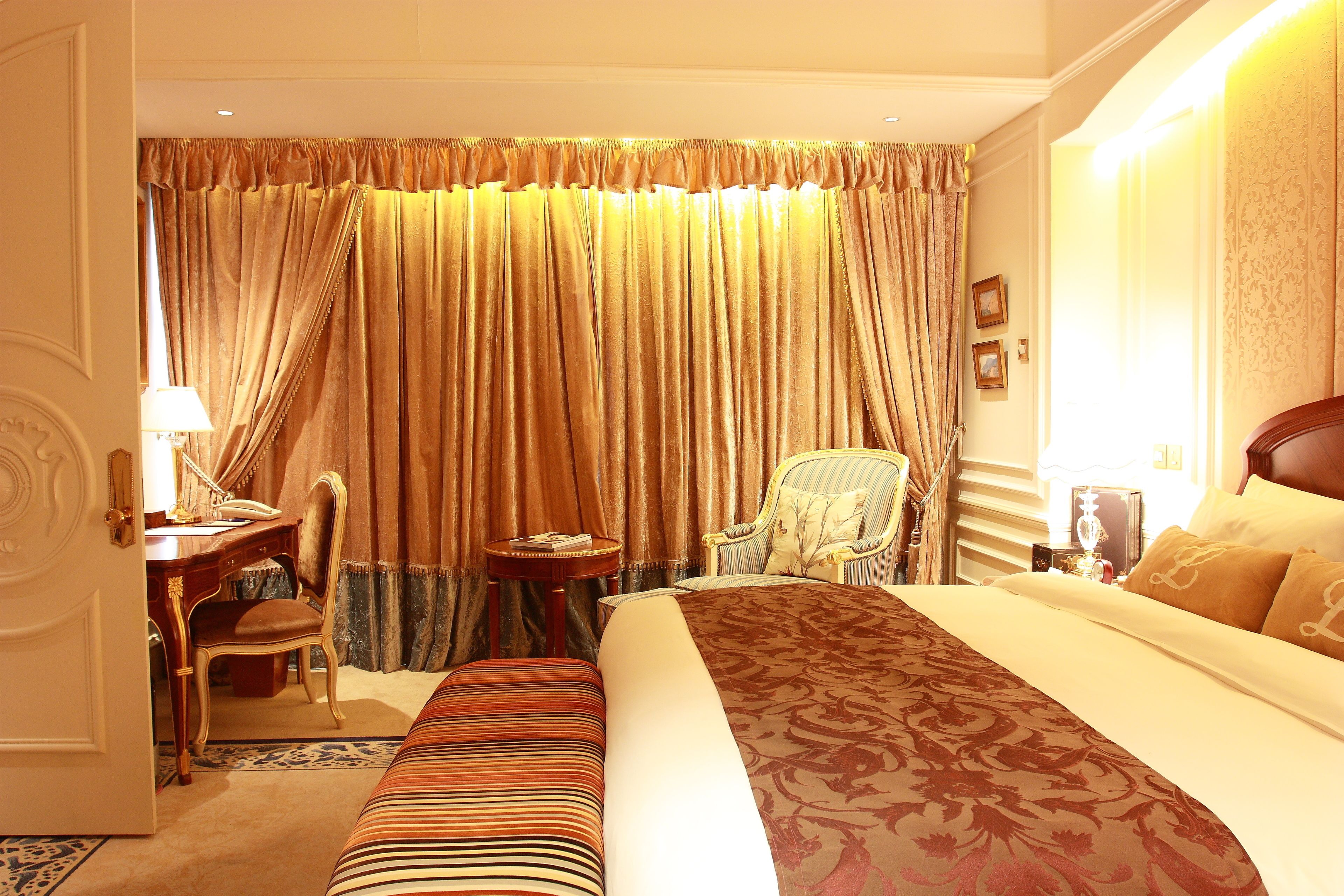 A hotel room with a large bed, a desk, a chair, and a small table.