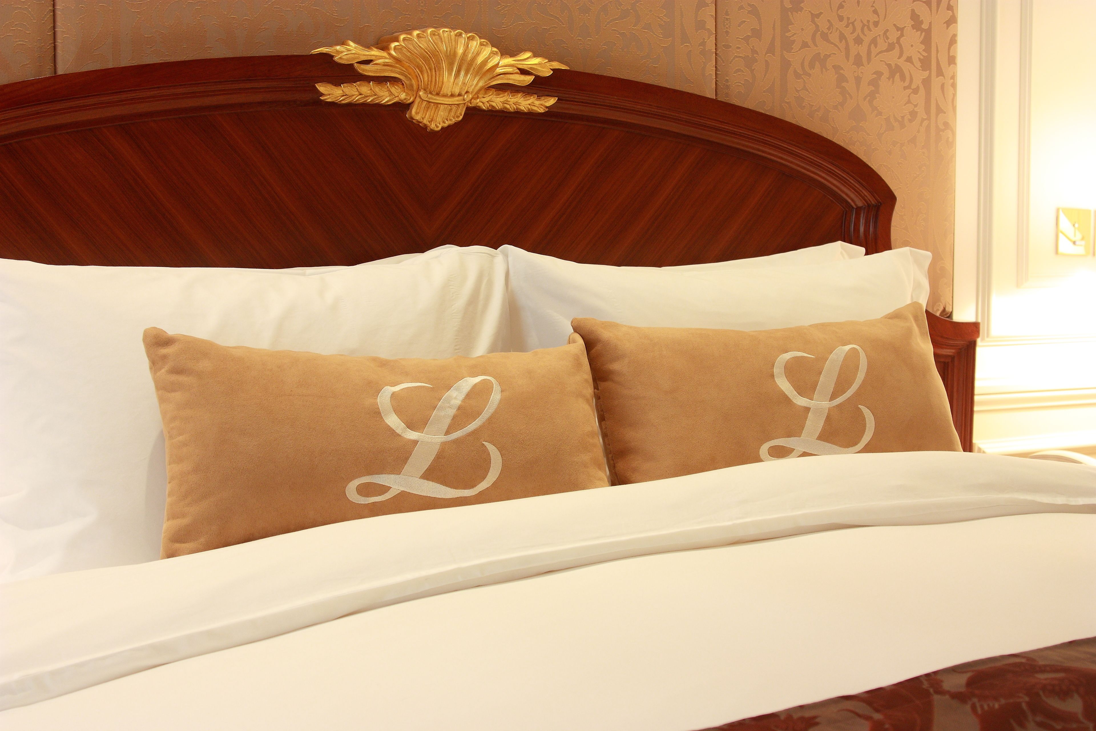 Een bed met witte lakens en twee bruine kussens met een monogram.
