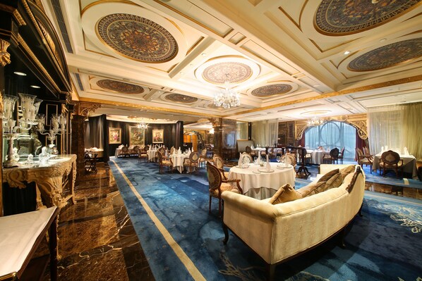 A luxurious hotel lobby with ornate ceiling designs, a central seating area, and a blue carpeted floor.