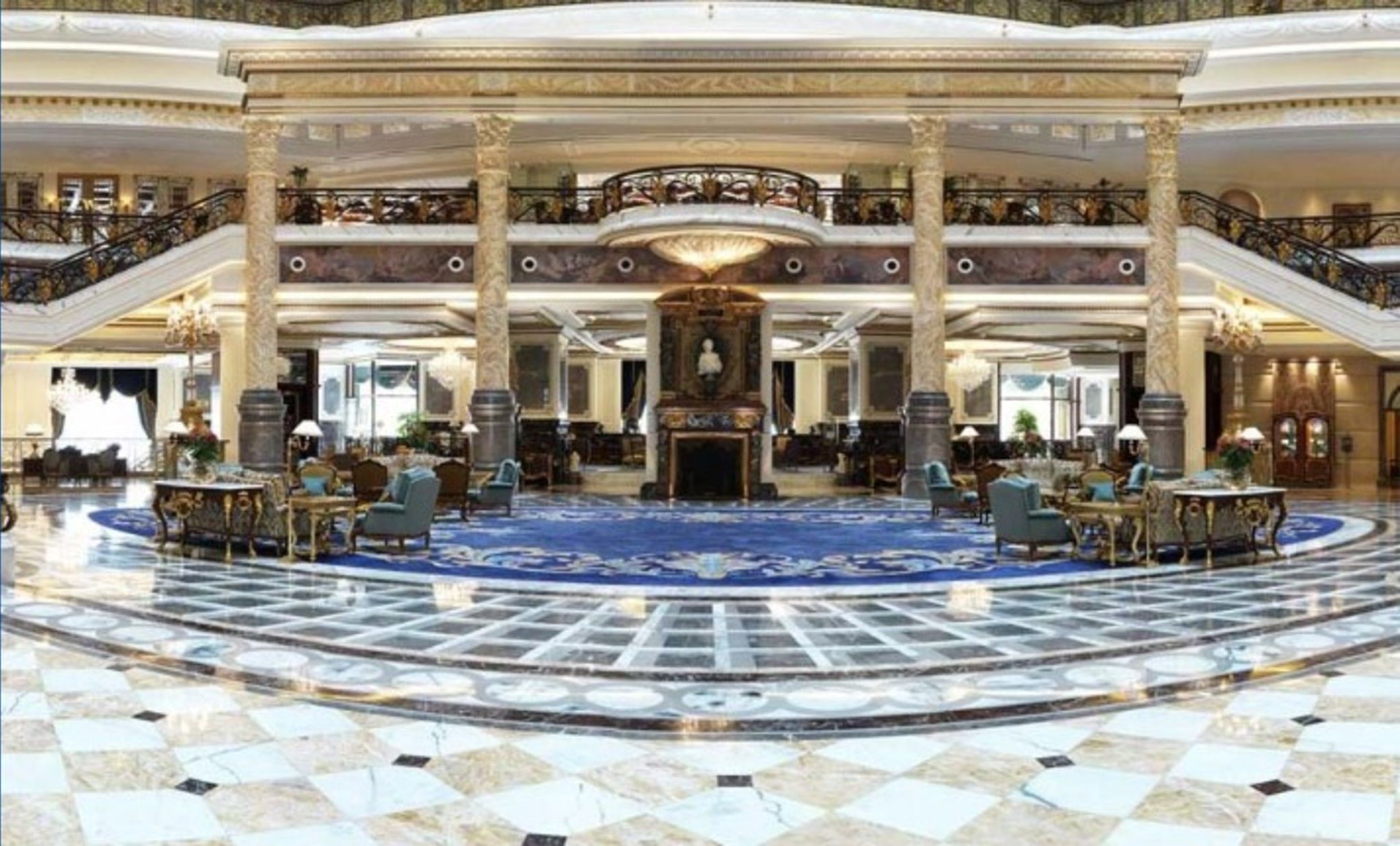 Un lobby espacioso con piso de mármol, columnas ornamentales y una chimenea central.